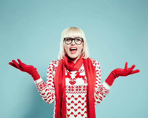 Excited blonde young woman wearing xmas sweater, scarf and gloves Portrait of excited blonde young woman wearing christmas sweater, red scarf and gloves, raising her hands. Studio shot, turquoise background. christmas nerd sweater cardigan stock pictures, royalty-free photos & images