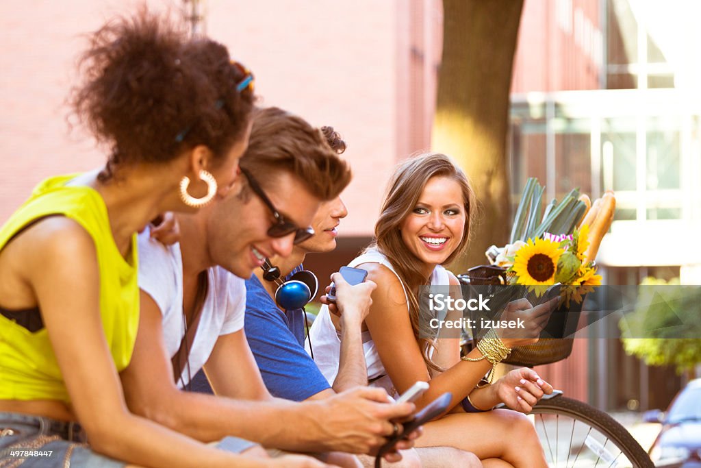 Urban young people Four young people using smart phones outdoors. 20-24 Years Stock Photo