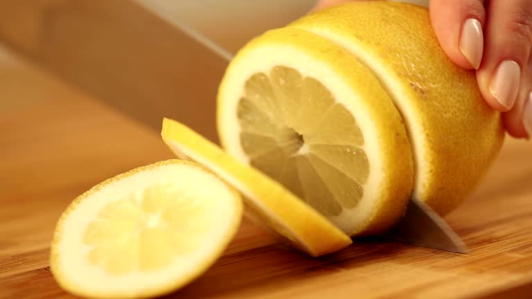 Cutting a lemon with a silver knife on a wooden plate.