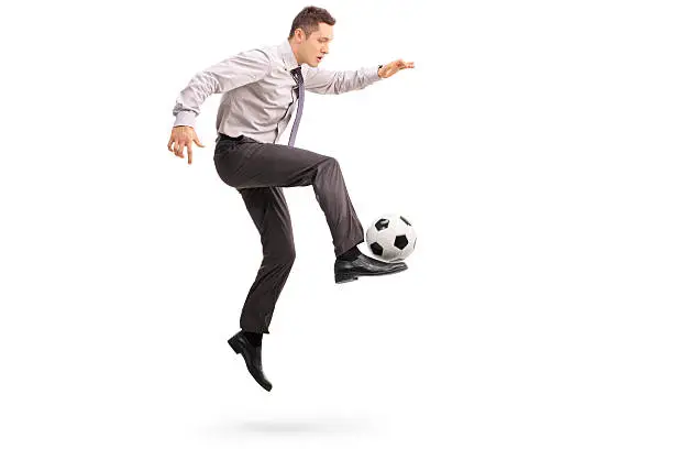 Full length profile shot of a young businessman playing football shot in mid-air isolated on white background