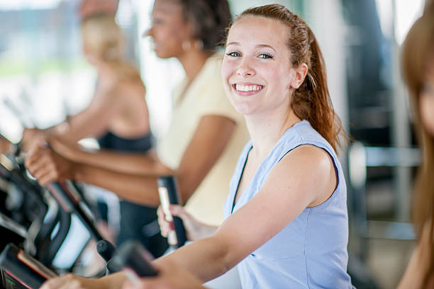 Teenage Girl Working Out A young woman is smiling and working out on the treadmill at the gym. community health center stock pictures, royalty-free photos & images