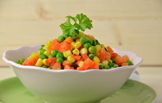 Colorful steamed vegetables - chopped carrot, corn, peas - in pink bowl