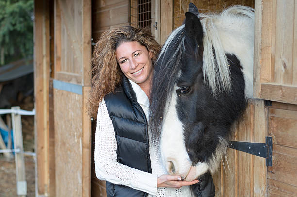 Standing in front of the barn and feeding the horse while looking in the camera