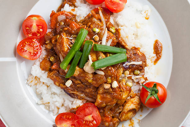 Szechuan chicken with white rice on a plate decorated with chive and cocktail tomato