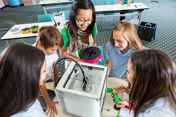 Teacher teaching students to load filament into 3D printer Young adult Asian woman is teaching private middle school class. Teacher is teaching students to load colorful rolls of filament in 3D printer in order to print objects they designed in class.Students are examining printer and are amazed by new technology. 3d printing filament photos stock pictures, royalty-free photos & images