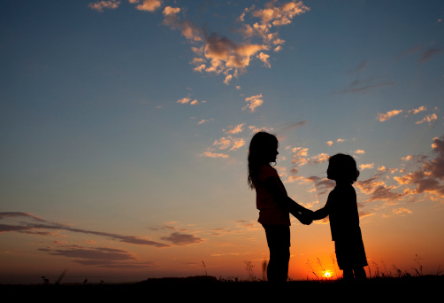 A silhouette of two children holding hands at sunset. Friendship concept.