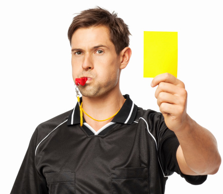 Portrait of young confident soccer referee whistling while showing yellow card isolated over white background. Horizontal shot.