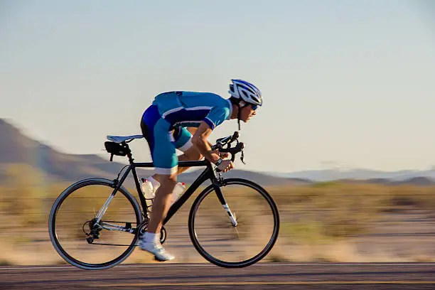 Cyclist sprinting past desert hills on a hot summers day.