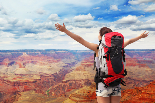 happy woman with backpack raised arm hands and looking to sky in grand canyon. asian