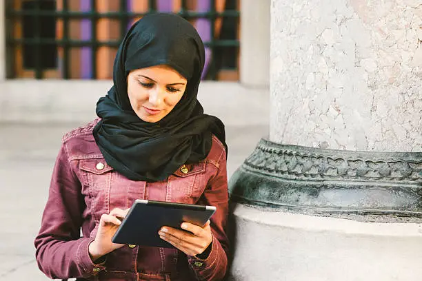Portrait of a young woman wearing headscarf using a tablet outdoors.