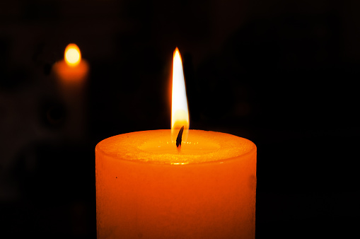 single burning candle on a dark background with reflection