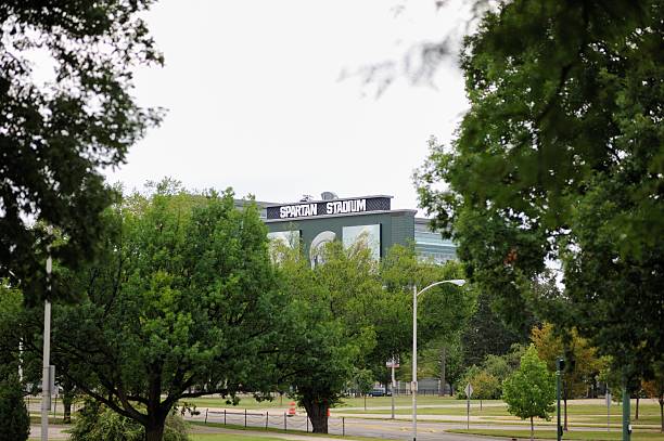 Spartan Stadium sign behind trees East Lansing, Michigan, USA - August 8, 2015: Photograph of sign on back of scoreboard at Spartan Stadium on the campus of Michigan State University in Lansing, Michigan. Image taken near the intersection of Red Cedar Road and West Shaw Lane.  michigan football stock pictures, royalty-free photos & images