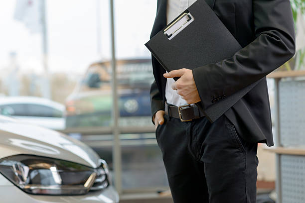 Salesman with clipboard is standing beside the car