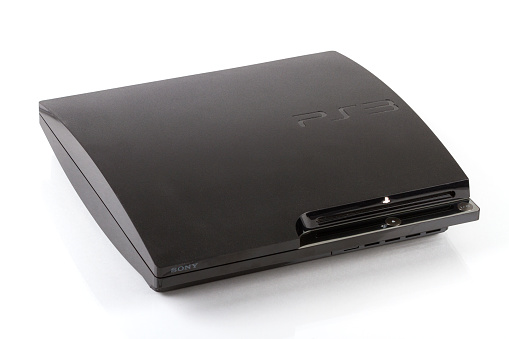 Calgary, Canada - July 4, 2011: Front angle view product shot of a Sony PlayStation 3 video game console, sitting on a reflective surface and isolated against a white background.