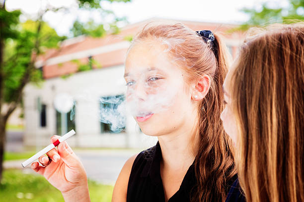preteen girl tries e-cigarette with her friend - vape stockfoto's en -beelden