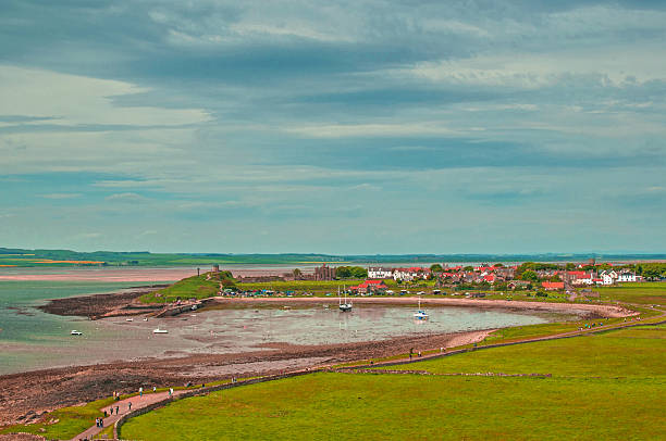 Bay Beach Sea and Boats Distant peaceful Village of Lindisfarne on Holy Island lindisfarne monastery stock pictures, royalty-free photos & images