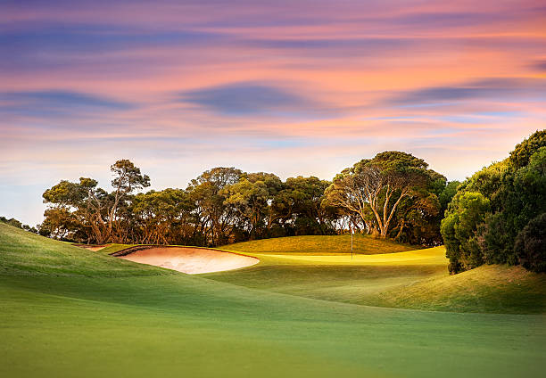 Golf Course at Sunset with light on the green Sun setting on a golf course with the green and pin in view surrounded by trees. golf course stock pictures, royalty-free photos & images