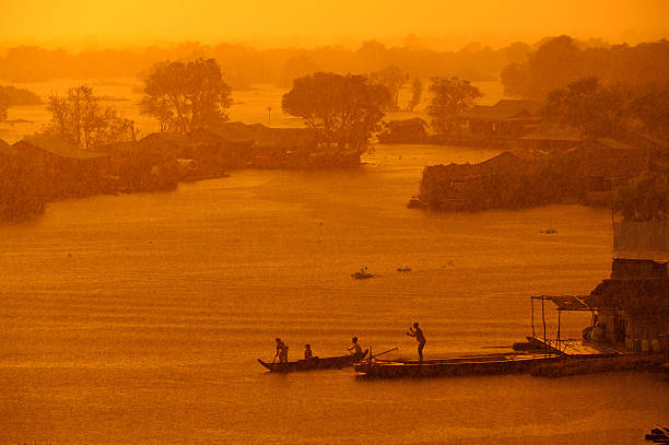 Monsoon rains start pouring as the sun sets on a floating village on the Tonle Sap Lake in Cambodia. A few people arrive at a wooden jetty by small boat.
