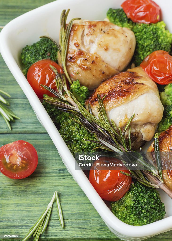 Chicken with vegetables Chicken legs with cherry tomatoes, broccoli, rosemary in a white bowl on the background of the tree. Backgrounds Stock Photo
