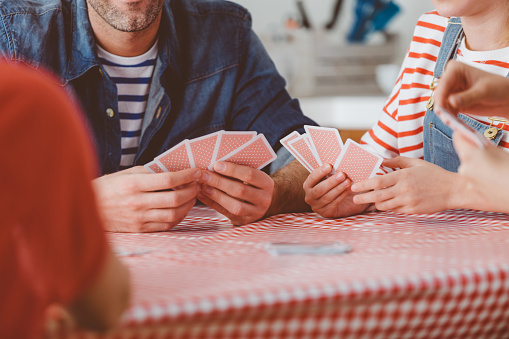 Family playing cards at home, sitting at the kitchen table. Close up of hands, unrecognizable people.