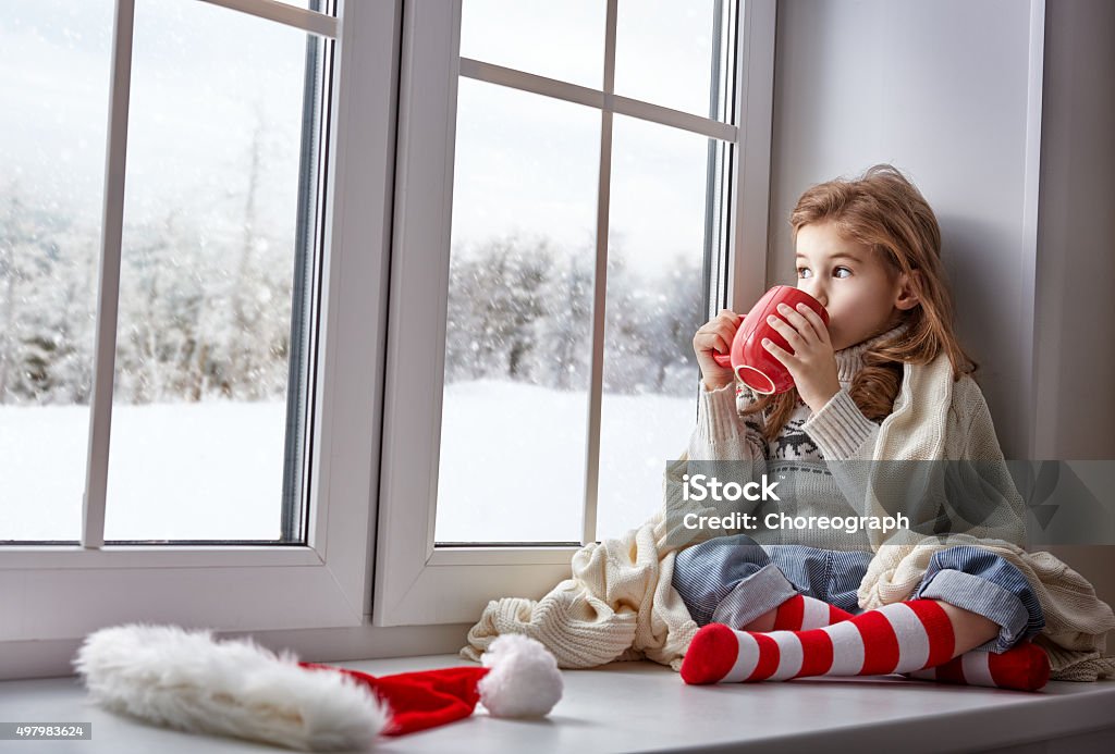 little girl sitting by the window little girl sitting by the window with a cup of hot drink and looking at the winter forest Window Stock Photo