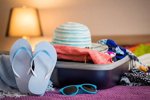 Open suitcase with clothing in the bedroom. Summer holiday concept.