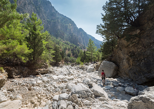 A woman on her way through the Samaria Gorge, Crete. The gorge is in southwest Crete in the regional unit of Chania and a major tourist attraction of the island  . It was created by a small river running between the White Mountains and Mt. Volakias. The gorge is 16 km long, starting at an altitude of 1,250 m (4100 ft.)at the northern entrance, and ending at the shores of the Libyan Sea in Agia Roumeli.