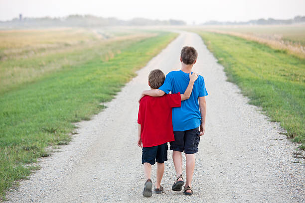 istock young boys arms around each other walking down road 497992219