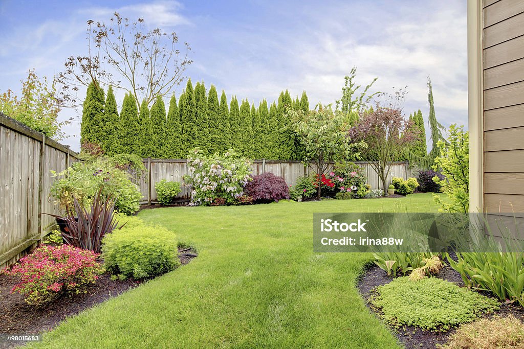 House exterior with landscape Fenced backyard. View of lawn and  blooming flower beds Yard - Grounds Stock Photo