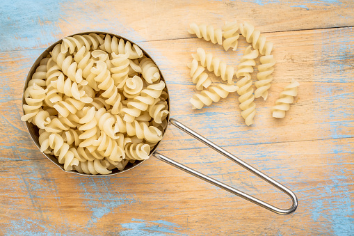 healthy, gluten free quinoa pasta (fusilli)  - top view of a metal measuring cup against painted wood