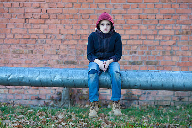 young homeless boy sits on a pipe with heating, city, street