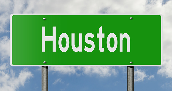 Green highway sign with clouds in the background showing the city Houston, Texas