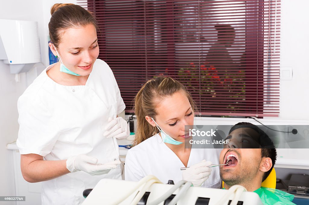 Dentist examines patient at clinic Female dentist with assistant examining the oral cavity of patient at dental clinic 20-29 Years Stock Photo