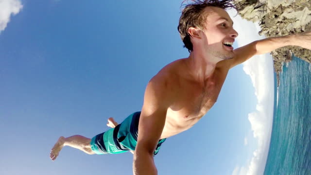 POV Slow Motion Cliff Jumping Backflip. Athletic Young Man Jumping From Cliff Into Ocean.
