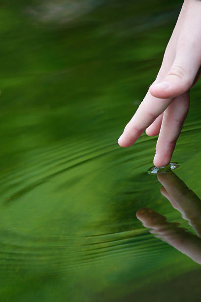 istock Fingertip radiating ripples and reflection on green pond 498048143