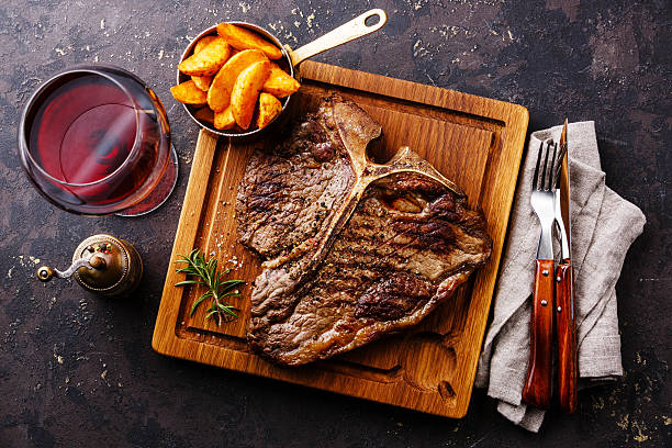 Grilled T-Bone Steak with potato wedges Medium rare Grilled T-Bone Steak with potato wedges and wine on serving board block on dark background t bone steak stock pictures, royalty-free photos & images