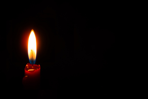 Red taper candle. Bright close-up photo shows flame transition from cool blue to white hot and reflections off of melted red wax.