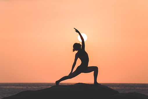 Warrior pose from yoga by woman silhouette on sunset