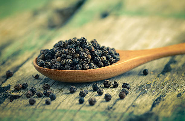 istock Whole black pepper on wooden spoon 498061052