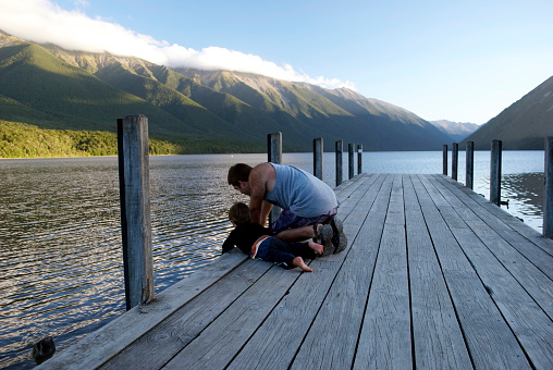 A Father and his Son look over the edge of the pier to the water below. Taken in the evening at Lake Rotoiti, nelson Lakes National Park, New Zealand's South Island.