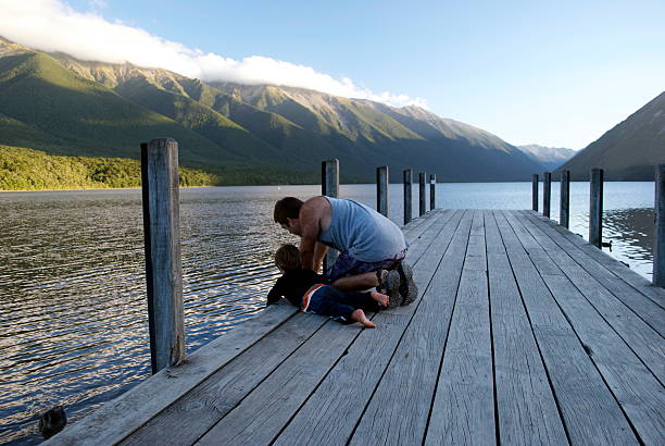 Father and Son on Pier, Nelson Lakes, New Zealand A Father and his Son look over the edge of the pier to the water below. Taken in the evening at Lake Rotoiti, nelson Lakes National Park, New Zealand's South Island. nelson city new zealand stock pictures, royalty-free photos & images