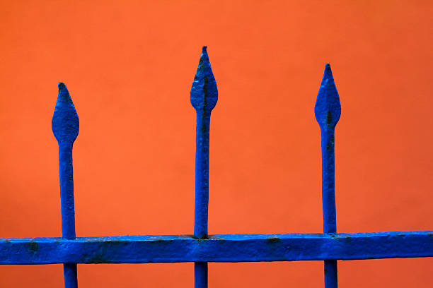 A sharp-pointed, cobalt-blue fence pops out against a flame-orange wall. Shot in the Aeolian Islands, Italy. Related concepts and ideas might be: sharp-edged, piercing, pointed, harsh, penetrating, to the point.