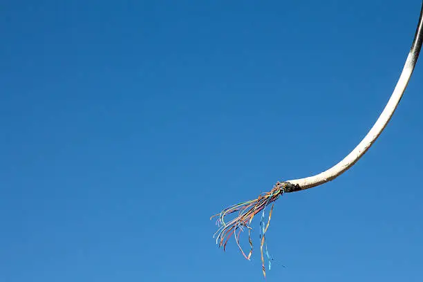 Image of a frayed and cut overhead wire against blue, clear sky.  The cable has multi-colored strands from the white painted rubber coated cable.