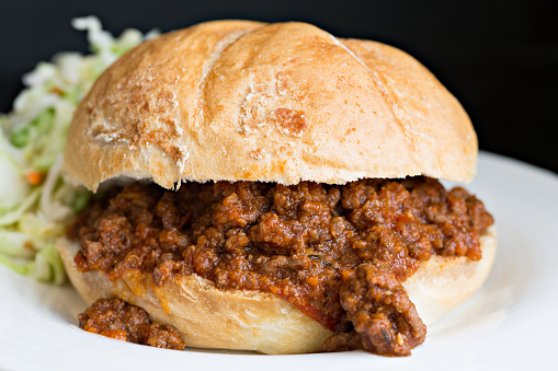 A close up shot of a plain sloppy joe with some cole slaw in the background.