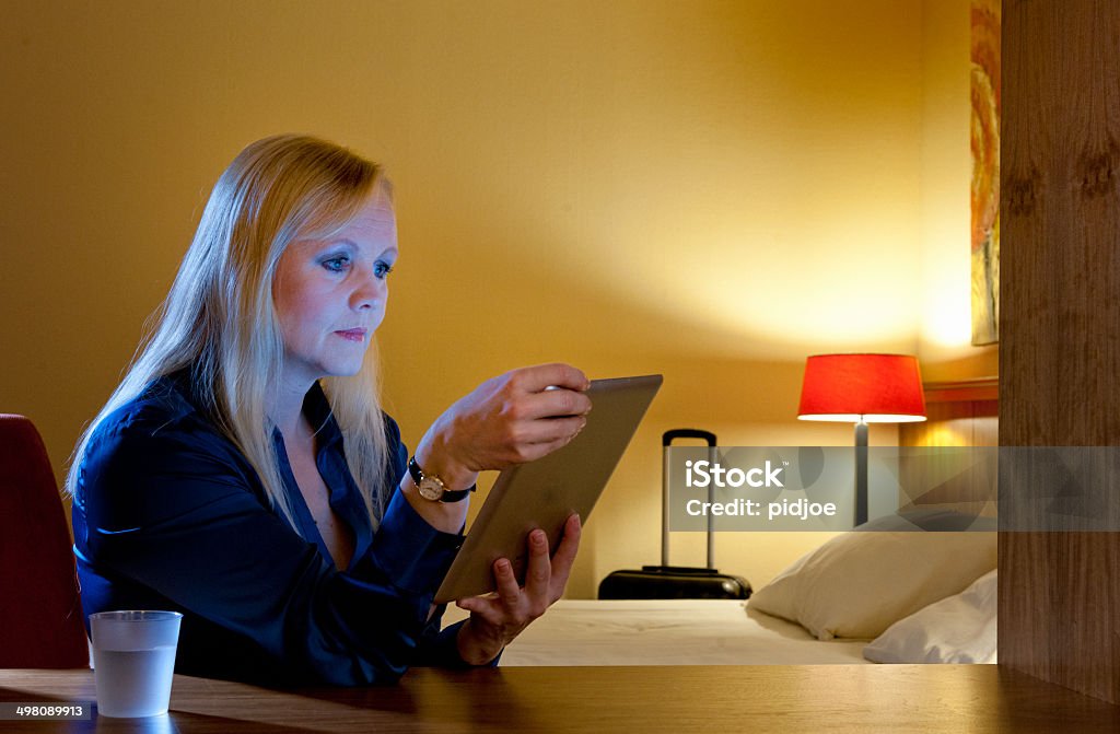 woman working in  hotel room using a tablet-pc Businesswoman or tourist sitting alone in a hotel room at night while travelling on a business trip using a tablet by lamp light to access the internet and multimedia via a wireless connection 40-49 Years Stock Photo