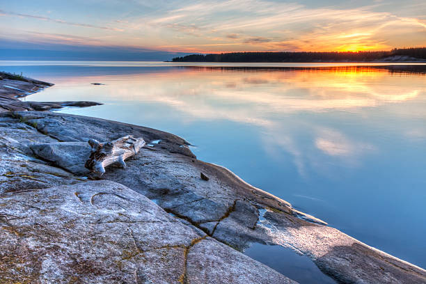 istock Granite shore with dry snag and sunset reflecting in water 498091711