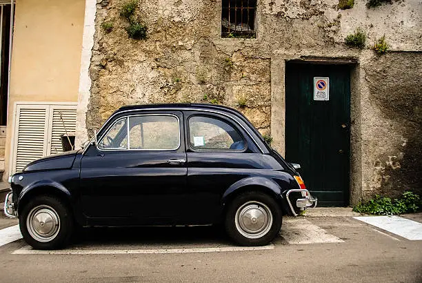 Old Fiat 500 parked outside an old stone house in Italy,