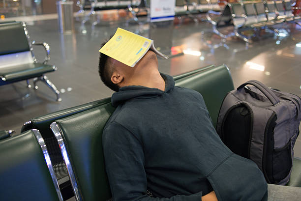 istock Young man sleeping in the airport with book on face 498111888