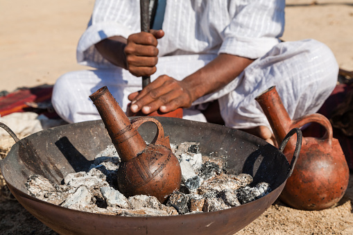 Marsa Alam, Red Sea/ Egypt OCTOBER 31: Coffee clay pot called fakhara in foreground while unidentified Bedouin young man from Bishari Tribe grind coffee beans, to make fresh Bedouin coffee called gabana in Characters of Egypt festival 2015.