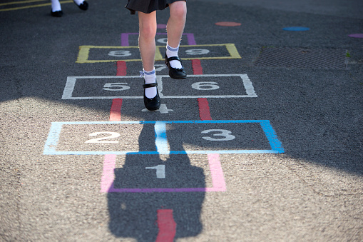 Schoolgirl playing hopscotch in the playground. Only seen from below the waist